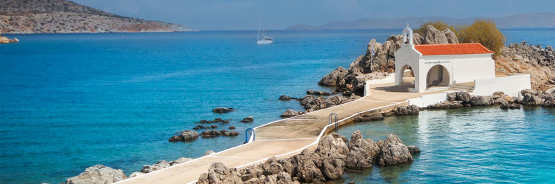 A whitewashed chapel on a rocky islet in a calm blue Greek bay